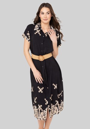 Robe noire à manches courtes avec broderie florale beige, ceinture à la taille. Comprend une fente à l'ourlet.