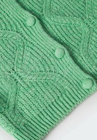 Detailní záběr na světle zelenou pletenou tkaninu s texturovanými vzory listů a třemi odpovídajícími knoflíky potaženými látkou.