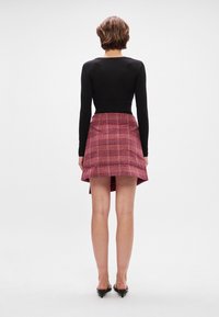 Melnā garo piedurkņu blūze kombinēta ar sarkano svītraino svārku ar platu apakšmalu un teksturētu audumu. Modelis valkā melnas augstpapēžu kurpes.