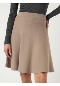 Une jupe mi-longue, longueur genou, en tissu beige clair doux avec une texture lisse et une ceinture élastique, portée avec un haut gris ajusté à manches longues.