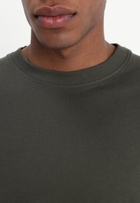 Sudadera de color verde con canalé que presenta un cuello redondo y una textura suave, ajustada alrededor del área del cuello.
