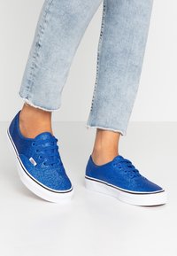 Sneakers blu glitter con design bassissimo, dotati di suole in gomma bianca e dettagli neri. Lacci e parte superiore in materiale glitter coordinato.