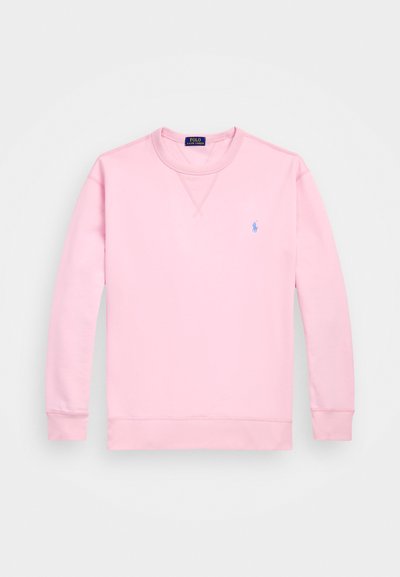 Svetlo roza pulover s krojnim ovratnikom, izdelan iz mehkega materiala. Žešvane manšete in roba, s malim modrim logo na levi strani prsnega dela.