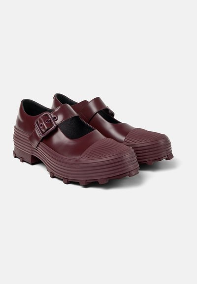 Maroon rubber shoes with a strap and buckle, featuring a textured, ridged toe and a thick, durable sole with spikes for traction.