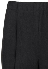 Zwarte geribbelde gebreide broek met een elastische tailleband en subtiele plooien, die een gestructureerd oppervlak benadrukken. Geen zichtbare zakken.