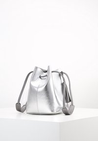 Sac seau en cuir argenté avec une fermeture à cordon et des accents gris. Texture lisse, forme arrondie et détail de pampille sur le côté.