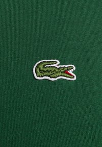 Tejido de punto verde con un pequeño logo de cocodrilo bordado en verde, contorneado en blanco y rojo en la boca.