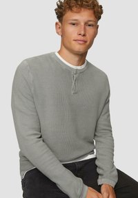 Graues, strukturiertes Langarm-Henley-Shirt mit rundem Halsausschnitt und Knopfleiste, über einem weißen Rundhalsausschnitt-T-Shirt getragen.