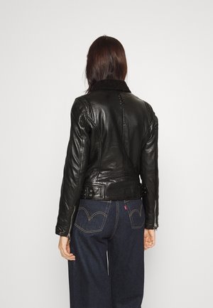 Giacca di pelle nera con colletto in shearling, design aderente e dettagli con fibbie, abbinata a jeans a gamba larga blu scuro.
