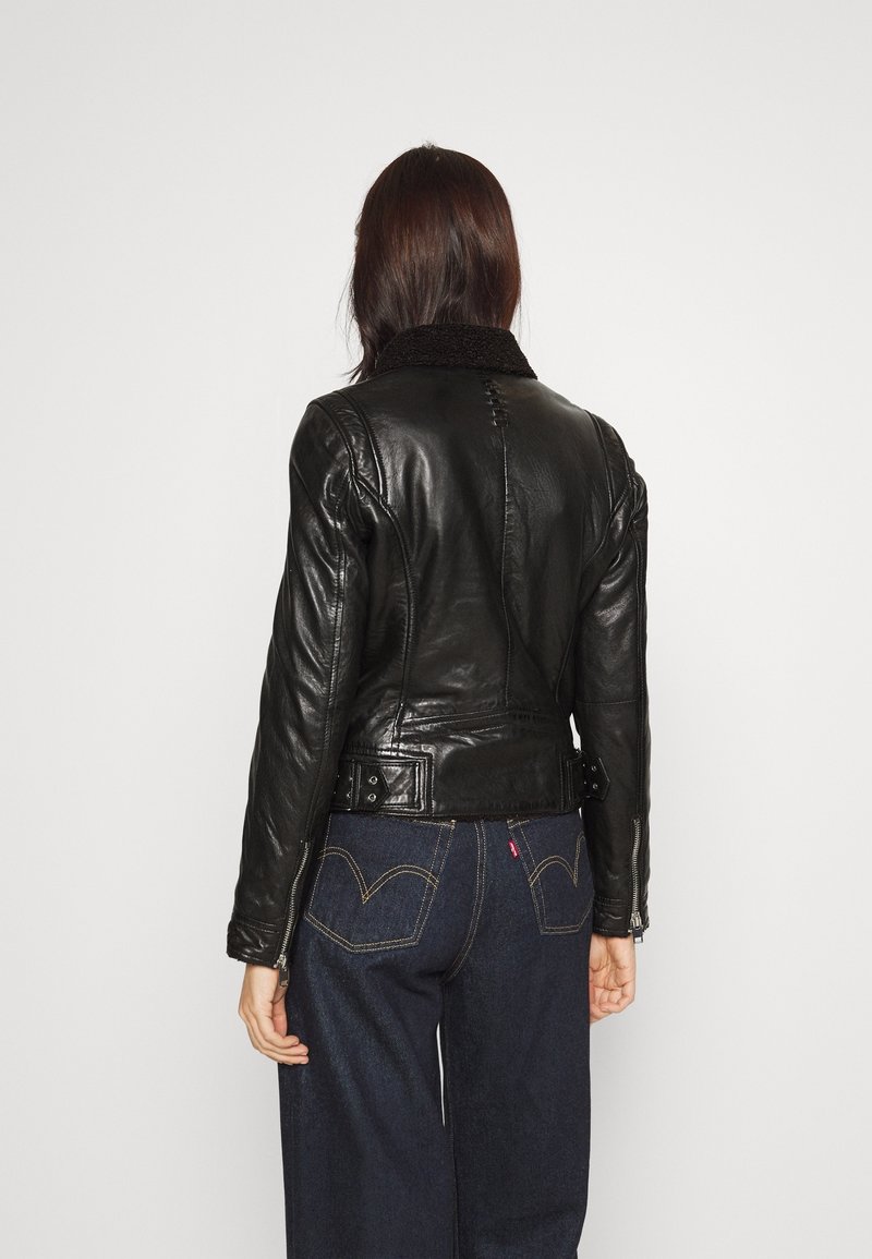 Zwarte leren jas met een schapenvacht kraag, getailleerd ontwerp en gespsieraden, gecombineerd met donkerblauwe wijde broek.