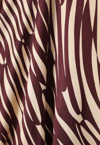 Burgundia ja kreemi zebra trükkiga kangas, millel on sile tekstuur ja kõverad, julged jooned, mis loovad silmatorkava mustri.