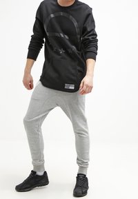 Svart långärmad sweatshirt med en stor grafisk design, tillsammans med ljusgrå tapered joggers och svarta sportskor.