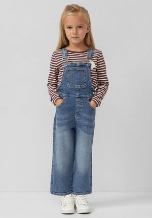 Denim tuinbroeken met een losse pasvorm, verstelbare bandjes, voorzakken en een bloemaccent, gecombineerd met een gestreept shirt met lange mouwen en witte sneakers.