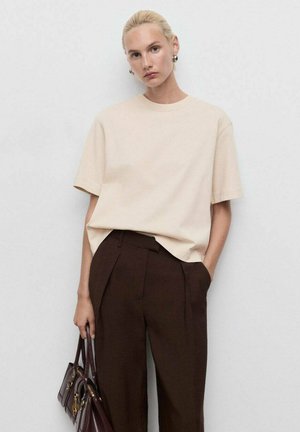 T-shirt beige à manches courtes avec un col rond, associé à un pantalon taille haute marron foncé ; tissu lisse et coupe décontractée. Sac à main marron.