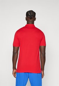 Rode polo shirt met een strak ontwerp, korte mouwen en een zachte textuur. Draag het met blauwe shorts; bevat een discrete label aan de zijkant.