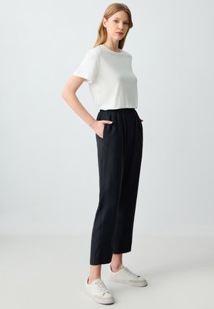 Witte top met korte mouwen gecombineerd met losse zwarte broek met elastische tailleband en zijzakken, gedragen met lichtgekleurde sneaker.