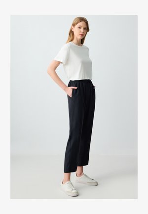 Biała koszulka z krótkim rękawem zestawiona z luźnymi czarnymi spodniami na gumce z bocznymi kieszeniami, noszona z jasnymi trampkami.