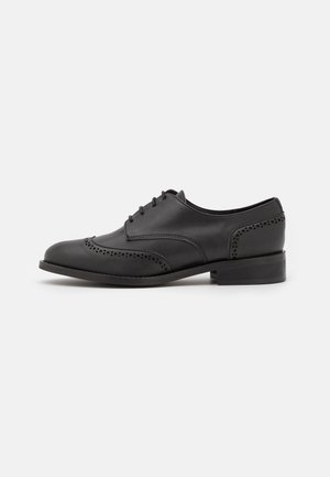 Czarny męski oxford z skóry, z ażurowymi perforacjami w stylu brogue, wiązany na sznurowadła, z niskim, warstwowym obcasem, pokazany z boku na białym tle.