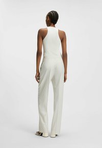 Wit geribd jumpsuit met verticale strepen, met een mouwloos ontwerp en een aansluitende taille. Lange, rechte pijpen met een nette afwerking.