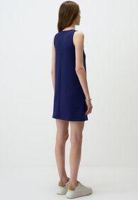 Ärmelloses navyblaues Kleid mit geradem Schnitt, das eine glatte Textur und minimalistisches Design aufweist. Getragen mit hellen Sneakers.