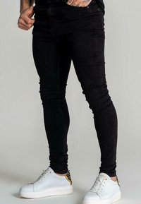 Svarta tajta jeans i denim med en figurnära design, slät textur och framfickor, kombinerade med vita sneakers.