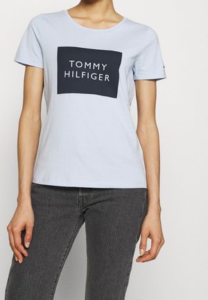 Lyseblå bomulds-T-shirt med rund halsudskæring, prydet med en mørkeblå rektangulær grafisk illustration med teksten "TOMMY HILFIGER" i hvid.