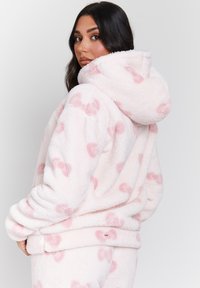 Felpa con cappuccio rosa in fleece, con una texture morbida, caratterizzata da un cappuccio e motivi a cuore rosa. Include un'etichetta cucita all'orlo.