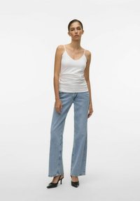 Canotta bianca aderente, jeans a gamba larga blu chiaro e tacchi a punta nera. Tessuto morbido, linee nette ed elementi di design minimalisti.