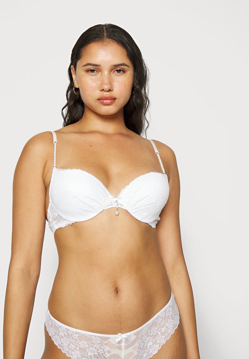 Witte kanten bh met gevoerde cups, geschulpte randen en een parelaccent in het midden, gecombineerd met bijpassende kanten bikini-slip.