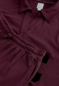 Bordeauxfarbendes Poloshirt mit V-Ausschnitt und passenden dehnbaren Jogginghosen. Weicher Stoff mit elastischem Bund und schwarzen Akzentdetails.