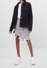 Svart denimjacka med en plyschkrage, parat med en sliten grå denimkjol med fransade kanter, bärs med vita sneakers.