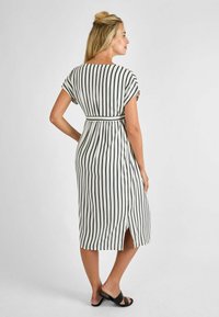 Abito a strisce bianco e nero, lungo fino al ginocchio, con maniche corte, vita cinte e uno spacco laterale. Realizzato in tessuto leggero.