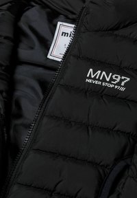 Svart puffjacka med kviltad textur; har dragkedja fram och vit tryckt logotyp "MN37 NEVER STOP 97" på framsidan. Inre tyg är slätt.