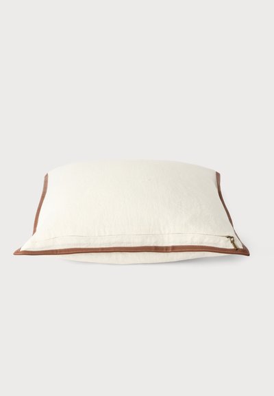 Oreiller rectangulaire blanc avec bordure marron et fermeture éclair visible sur un fond uni gris clair.