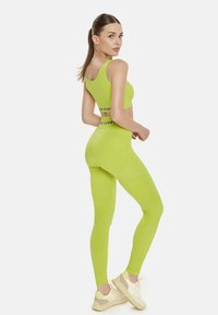 Top sportiv scurt de culoare verde neon și colanți din material elastic, având o talie neagră branduită și pantofi sport ușori.