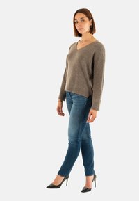Maglione a collo a V, marrone e texturizzato, con maniche lunghe, abbinato a jeans blu aderenti e tacchi alti neri. Design semplice; palette di colori neutri.