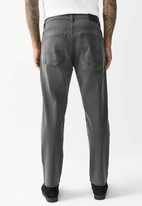 Grå denimjeans med lige ben, der har fem lommer, synlige syninger og et sort båndmærke i taljen. Båret med sorte sko.