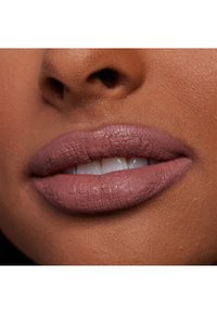 Matowy szminka w kolorze mauve na pełnych ustach z delikatną teksturą. Zbliżenie podkreśla neutralny odcień skóry i lekki uśmiech.