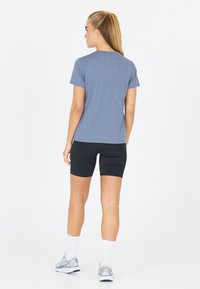 Sininen kanervapaitainen T-paita lyhyillä hihoilla, yhdistettynä mustiin kompressioshortseihin. Mallilla on valkoiset urheilusukat ja harmaat juoksukengät.