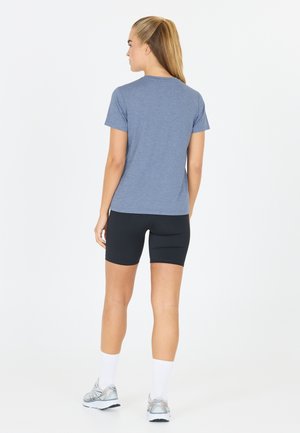 T-shirt bleu en bruyère à manches courtes, associé à un short de compression noir. Le modèle porte des chaussettes de sport blanches et des chaussures de course grises.