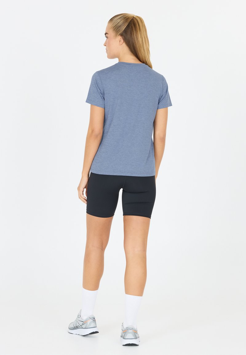 Sininen kanervapaitainen T-paita lyhyillä hihoilla, yhdistettynä mustiin kompressioshortseihin. Mallilla on valkoiset urheilusukat ja harmaat juoksukengät.