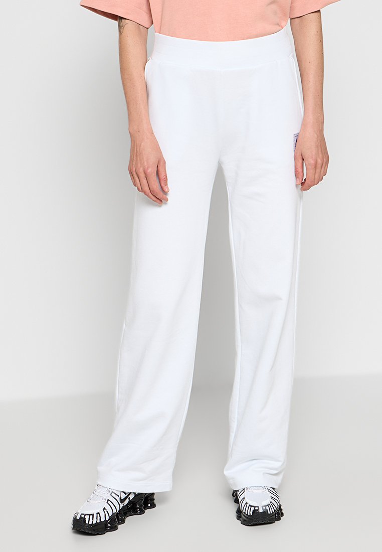 Białe bawełniane dresy o luźnym kroju, z wysokim pasem i kieszeniami bocznymi, w połączeniu z czarno-białymi butami sportowymi w wzory.