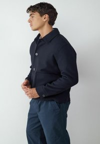 Granatowa kurtka z kołnierzykiem, z przodu zapinana na guziki, z bocznymi kieszeniami. Wykonana z gładkiego materiału o luźnym kroju.