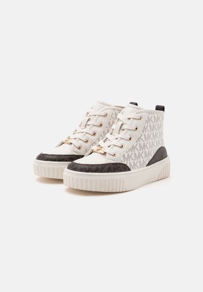 Ζευγάρι λευκά sneakers ψηλού τύπου με μπεζ και καφέ μοτίβο λογοτύπου MK, λευκά κορδόνια και χοντρές λαστιχένιες σόλες σε απλό φόντο.