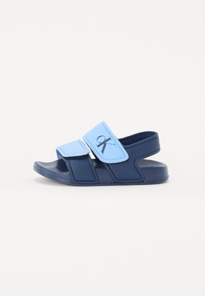 Navy blue sandals with light blue Velcro straps, a textured outsole, and a small logo at the front. Open-toe design and adjustable fit.