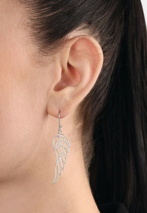 Pendientes en forma de ala plateada con un intrincado diseño recortado, colgando de un aro simple. Los pendientes cuelgan ligeramente delante de la oreja.