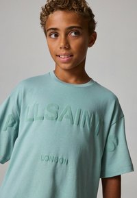 Piparmētru zaļš oversize T-krekls ar uzrakstu "ALLSAINTS" izvirzītā burtu formā un "LONDONA" iepresēts apakšmalā. Mīksta kokvilnas auduma.