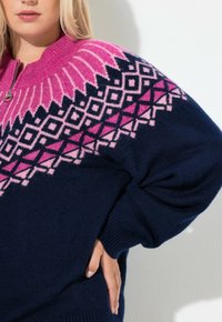 Maglione blu navy a maglia con collo alto, caratterizzato da un motivo geometrico rosa al bordo del collo e alle maniche superiori, con polsini a costine.
