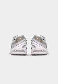 Baskets de sport en blanc, gris et or avec une tige en maille, un talon rembourré et une unité d'air visible dans la semelle. Design arrondi et élégant.