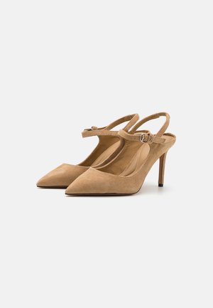 Beżowe zamszowe obcasy typu slingback z noskami w szpic, paskiem na łuku stopy oraz 10-centymetrowym obcasem w stylu stiletto. Gładka tekstura i minimalistyczny design.